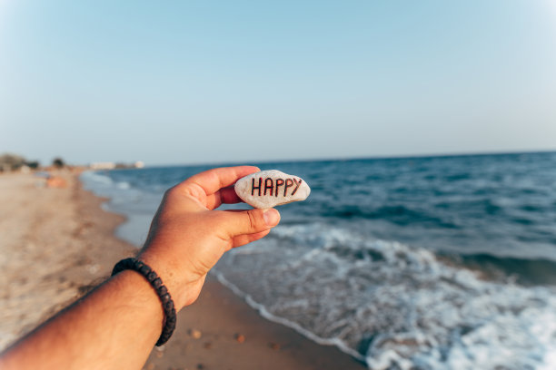 男人拿着写着“幸福”的石头在海滩上图片下载