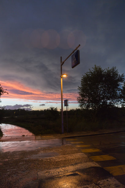 戏剧性的天空后一场风暴，植被在背光和街道在黑暗与街灯图片下载