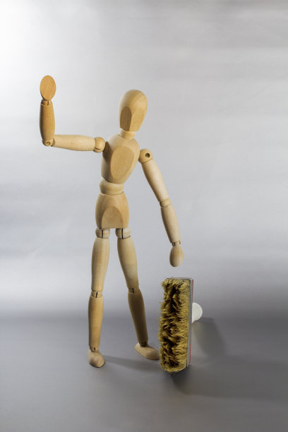 木娃娃对着镜头挥挥手，她的旁边立着一把宽刷子图片下载