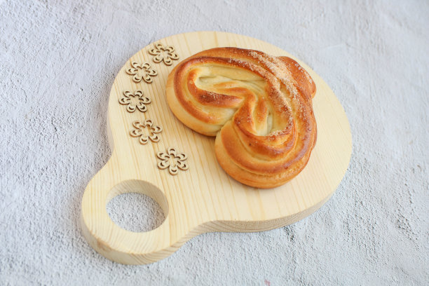 在灰色的背景上，心形面包放在一个圆形的木砧板上，侧视图，图片下载