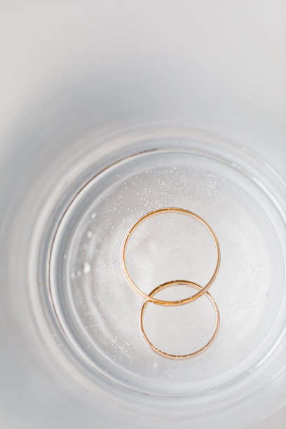 结婚戒指放在一杯水里。在一张白色的桌子上。图片下载