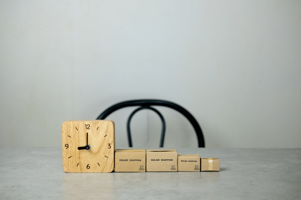 在办公室的桌子上有一个微型的棕色纸板箱和一个木制的时钟。概念电商和及时配送服务图片下载
