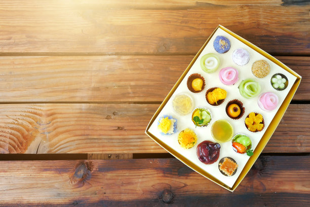 前视图。各种各样的泰国甜点(Khanom Thai)在一套顶部纸盒上的木制桌子。许多形状像一朵花，如此优雅美丽。图片下载