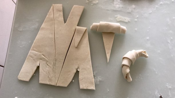 在烤盘上铺上准备烘烤的防油纸，面团被卷好并切成新月形的羊角面包图片下载