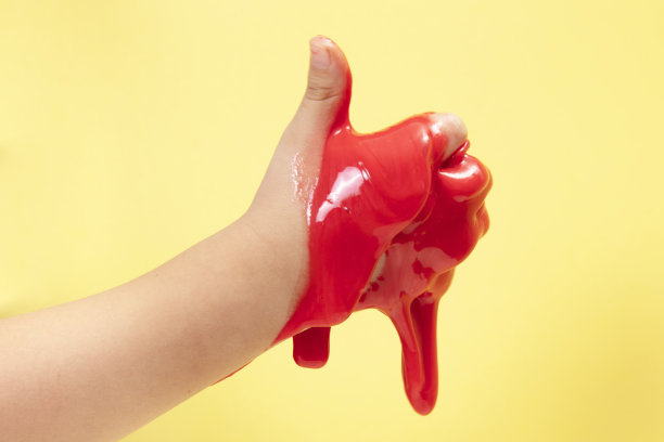 快乐的小男孩举起他的拇指玩霓虹灯红色黏液玩具在黄色波普艺术背景。图片下载