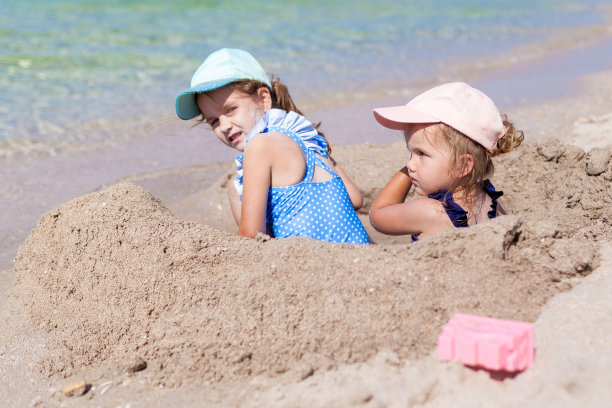 在一个阳光明媚的夏日，两个穿着泳衣和帽子的姐妹女孩在沙滩上玩玩具和沙子。有趣的海边家庭度假。孩子们在户外活动图片下载