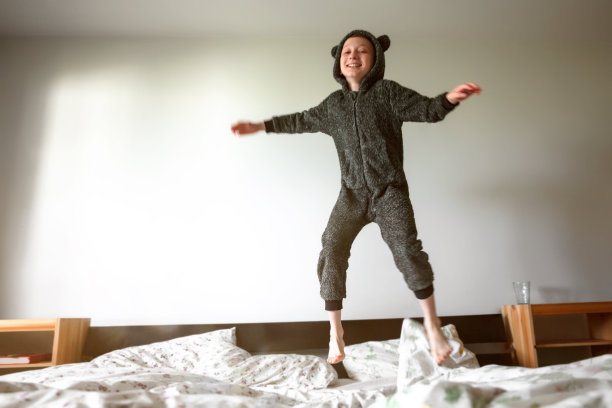 快乐有趣的小男孩在床上跳图片下载