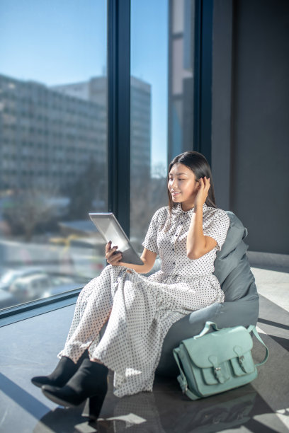 年轻的黑发女子坐在包椅上，一边看报纸，一边抚弄头发图片下载
