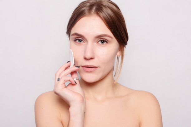 快乐的微笑美丽的年轻女子清洁皮肤的棉垫。图片下载