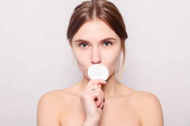 快乐的微笑美丽的年轻女子清洁皮肤的棉垫。图片下载