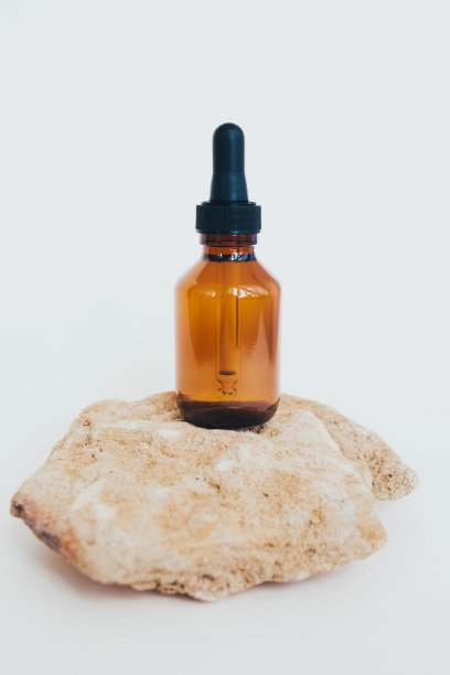 一个装有吸液器的瓶子，装满油或香精，放在一块石头上，背景很亮。侘寂的美学。自然学科。护肤精油。图片下载