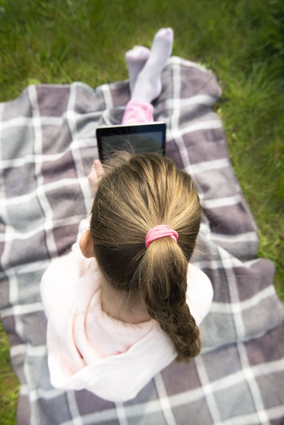 小女孩在花园里玩电子平板电脑。近距离图片下载