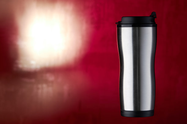 不锈钢咖啡杯正面视图。热旅行杯，用来喝热茶饮料。在一个红色模糊的背景。设计的空白。影棚拍摄。图片下载