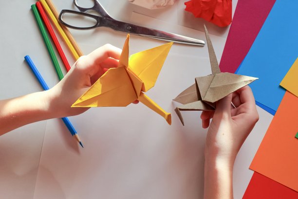 孩子们的手在白色的背景上用黄色的纸做折纸鹤。一步一步的折纸教程。孩子的创意观念，回到学校。图片下载