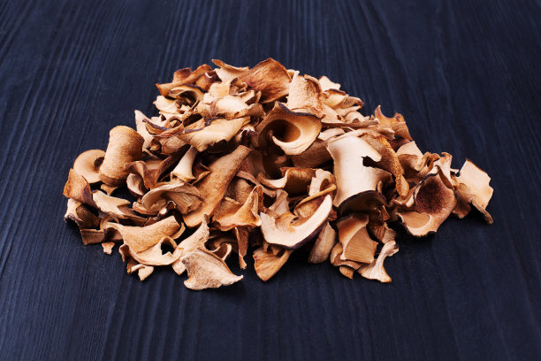 可食用的干蘑菇堆黑色木质背景近处，干牛肝菌堆黑色木质背景，切好的棕色牛肝菌帽，切好的小圆面包片，牛肝菌片，牛肝菌，切好的白色木耳图片下载