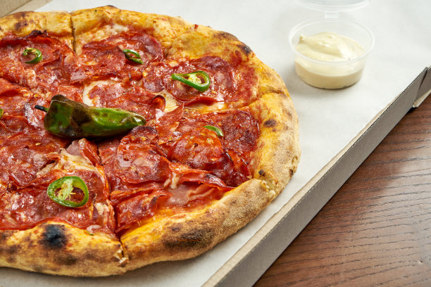 披萨外卖照片。披萨里有辣香肠腊肠，融化的奶酪装在纸盒里，配酱放在木桌上。近距离图片下载