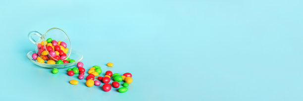 彩釉糖豆。杯盘上的玻璃杯，蓝色背景上散落着五颜六色的纽扣状巧克力，有复制空间。概念甜茶会。模板设计，文本横幅图片下载