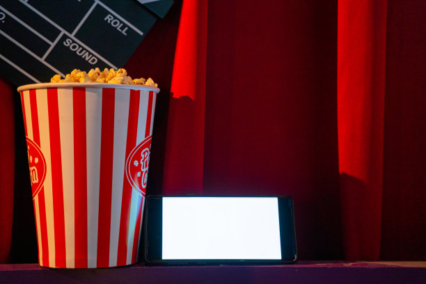 手机与空白色明亮的屏幕爆米花桶和电影拍板。在互联网手机上播放电视的概念。图片下载