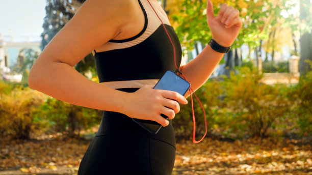 特写照片的年轻女子拿着智能手机在秋天公园跑步和听音乐图片下载