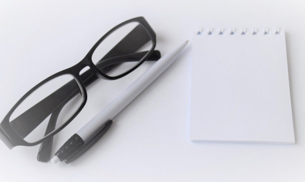 模糊的文本模板在一个白色背景的记事本上，与一个白色的笔和黑框眼镜躺在旁边图片下载