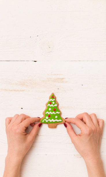 俯视图上女人的手拿着漂亮的圣诞饼干形状的树与装饰在白色的木制背景。假期。图片下载
