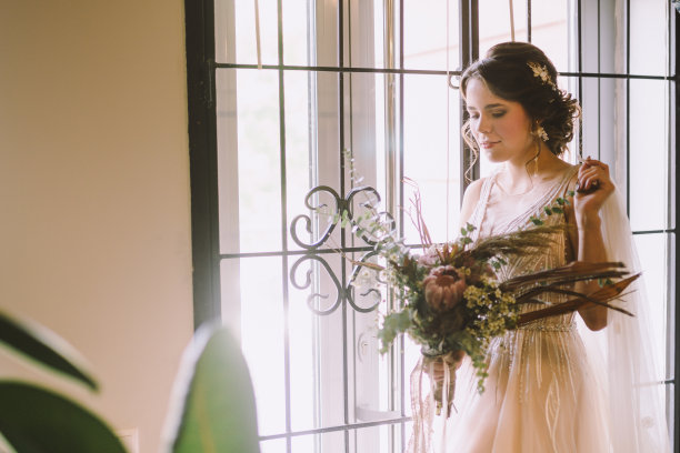 优雅的早晨的照片。的婚礼。新娘。准备。新娘拿着一束花靠近窗户。欧式婚礼。早晨新娘在婚礼当天等待新郎图片下载
