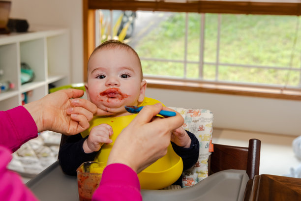 可爱的小男孩坐在喂食椅上，妈妈用勺子给他喂奶图片下载