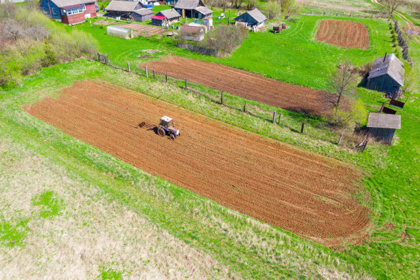在种蔬菜之前，拖拉机在村里犁地。天线高度的观点。图片下载