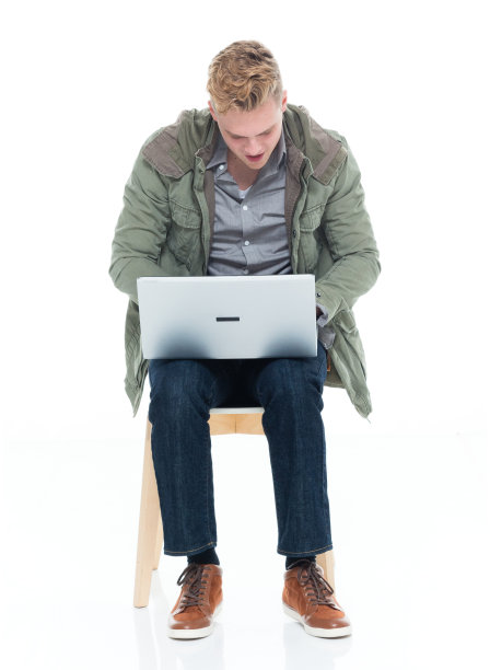 白人男性穿着夹克坐在白色背景前使用笔记本电脑图片下载