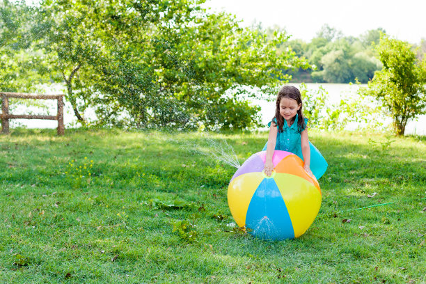 有趣的笑小女孩在一件衣服玩玩具球花园洒水车溅水有乐趣在后院在一个阳光炎热的暑假一天图片下载