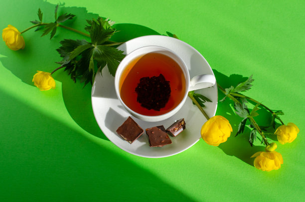 一杯红茶，几块巧克力，绿色背景上盛开着欧洲巨人的黄花。巧克力日和早茶。图片下载