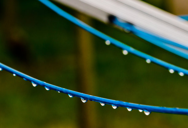 雨后，一件蓝色的衣服线在绿色的背景前，用许多雨滴在线上旋转。复古洗衣服的方式。图片下载
