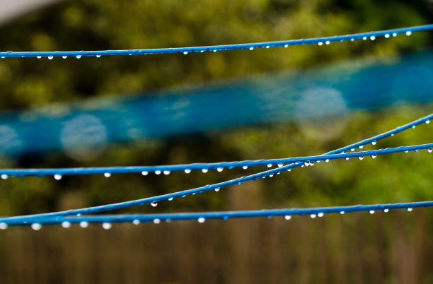雨后，一件蓝色的衣服线在绿色的背景前，用许多雨滴在线上旋转。复古洗衣服的方式。图片下载