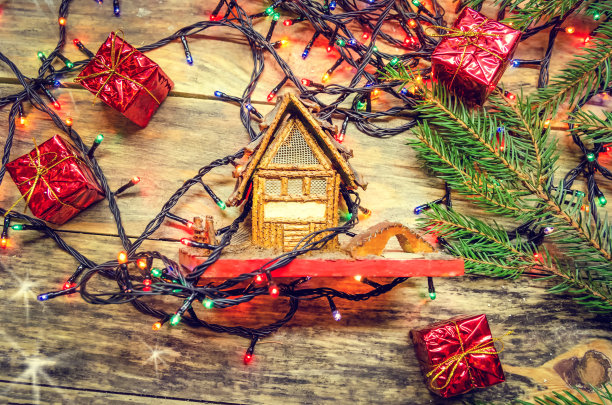 玩具屋上有一个木制背景包裹的圣诞花环，还有小礼物和圣诞树的树枝。美丽的圣诞背景，俯视图图片下载