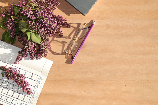 一个现代女性的桌面，家庭办公室，电脑，笔记本，丁香在阳光下的长阴影的桌子上。简约的经营理念，平铺，图片下载