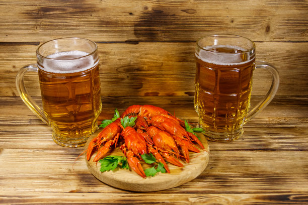木桌上放着煮小龙虾和两杯啤酒图片下载