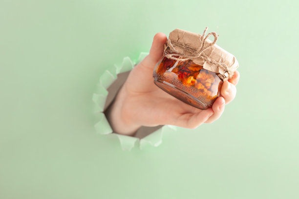 他的手拿着一罐蜂蜜和坚果，穿过被撕破的蓝色墙纸上的一个洞。图片下载