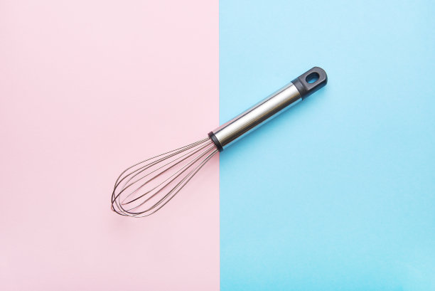 蓝色和粉色背景的金属丝搅拌器。金属丝搅拌器工具背景图片下载