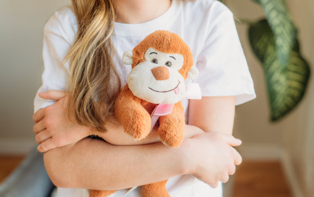 一个小女孩(脸不在照片中)双手交叉抱着她可爱的毛绒猴子。图片下载