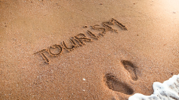 特写照片的两个脚印和字旅游铭刻在海滩上。旅游、旅行、旅行和旅行的概念。图片下载