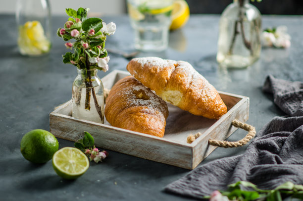 新鲜的羊角面包和柠檬水作为早餐。桌上放着春天的花。图片下载