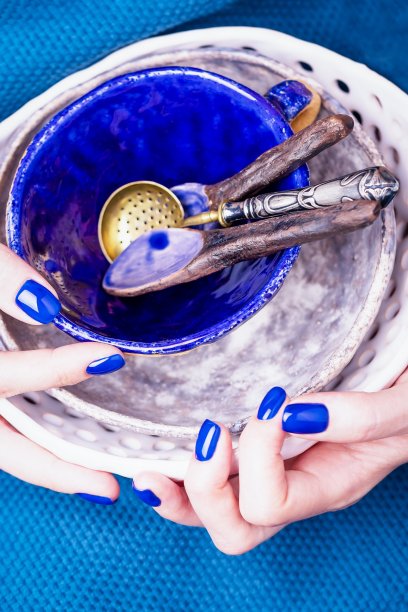 女性的手用亮蓝色修指甲拿着新的陶瓷餐具图片下载