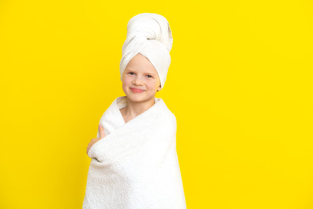 可爱的小白人女孩的肖像裹在白色毛巾与浴巾在头上在黄色工作室背景。水疗程序，沐浴纺织品图片下载