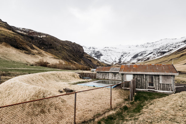 在白雪皑皑的群山映衬下，冰岛的老木屋和一个温泉池。山里有温泉的旅馆。图片下载