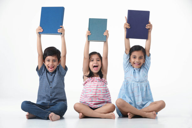 一群兴奋的学校孩子们，孩子们，男孩和女孩，坐着，用他们头上的书欢呼图片下载