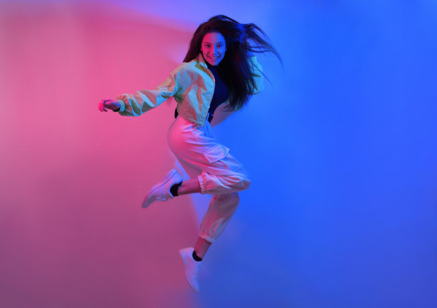 褐发女郎穿着霓虹灯跳舞，舞者穿着红蓝色。嘻哈女孩，派对，微笑。模型在飞行，跳跃。图片下载