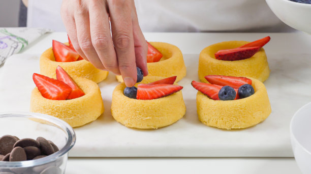 新鲜浆果，巧克力和鲜奶油的饼干蛋糕。女人准备甜点，迷你饼干杯草莓和蓝莓，靠近白色的背景图片下载