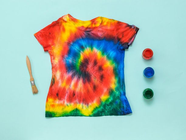一把刷子，三罐颜料，一件蓝色背景的扎染t恤。平的。图片下载