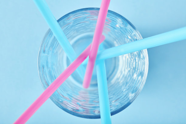 蓝色背景的空杯子里的粉色和蓝色塑料吸管图片下载