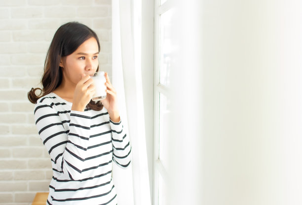 亚洲美女朋友们站着，捧着一杯牛奶，在早晨关上窗户和窗帘与拷贝空间。图片下载